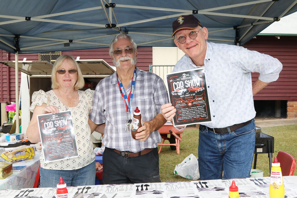 Pauline & Syd Norman & Adrian Butcher from TDCA - at the Tamborine Community Country Markets - holding posters for the upcoming Car Show